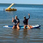 Usuari d'APASA i monitor asseguts sobre una taula de paddle surf a la platja